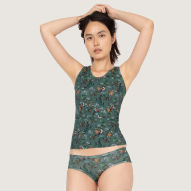 Eine junge Frau faltet die Hände hinter ihrem Kopf. Sie trägt ein Tanktop und den dazu passenden Hipster von Frija Omina im Dekor Ginko.